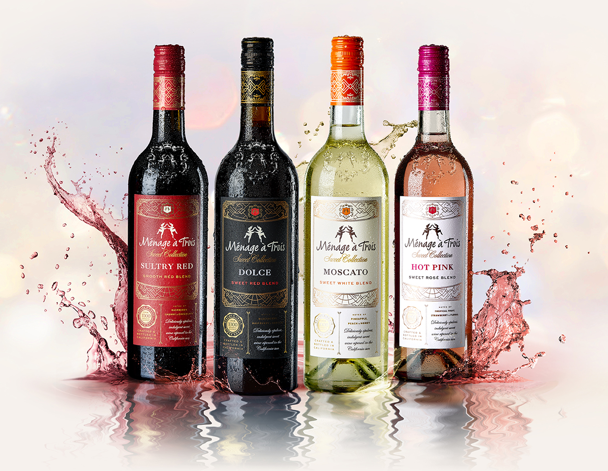 lineup of four menage a trois bottles from the sweet collection with splashed water underneath