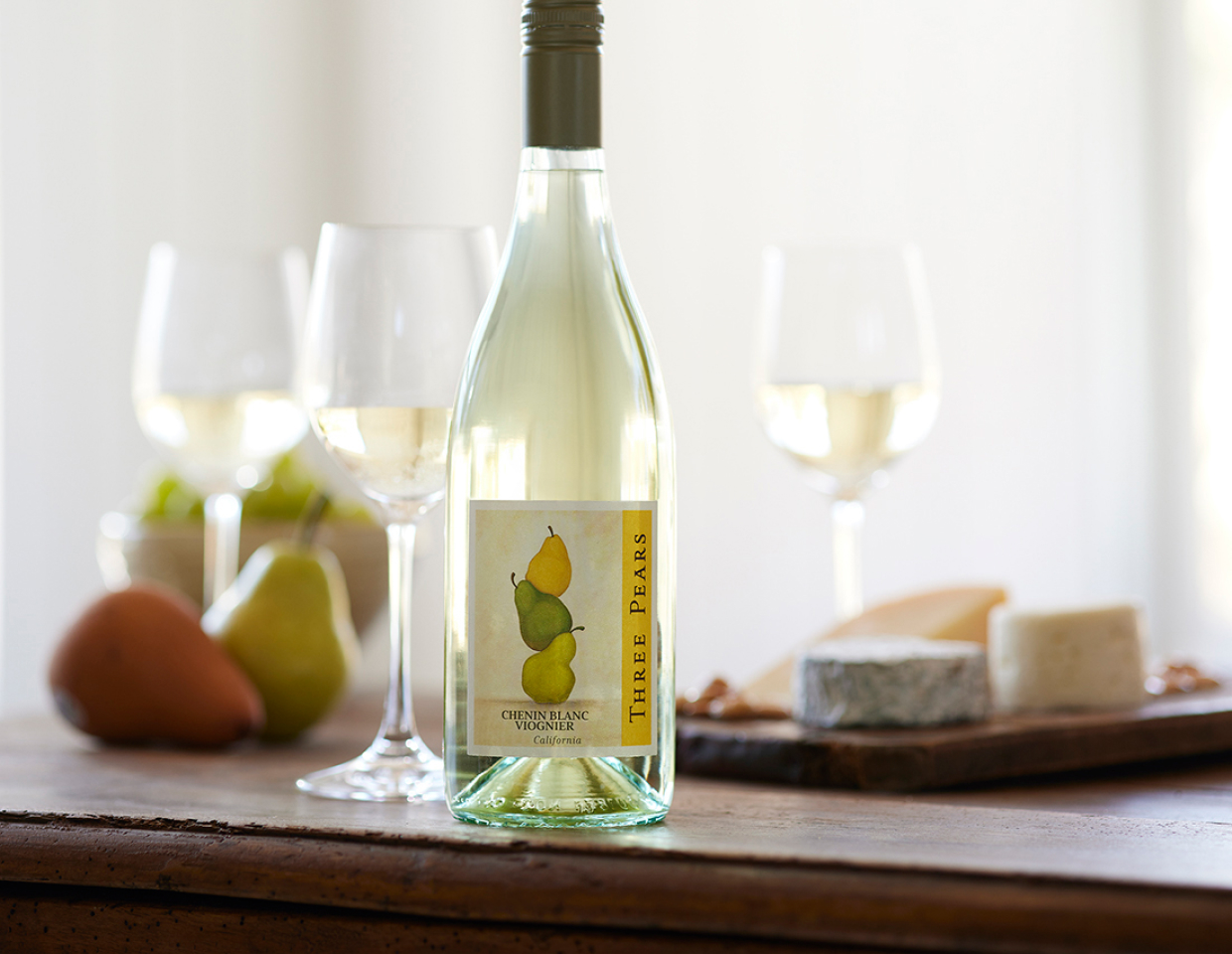 Bottle of Three Pears chenin blanc viognier on a table with glasses of wine, cheese, and fruit.