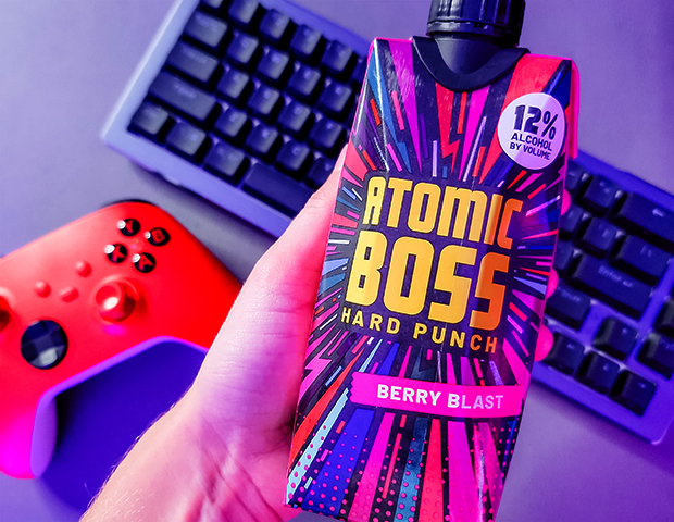 hand holding an Atomic boss berry blast over a keyboard and gaming controller