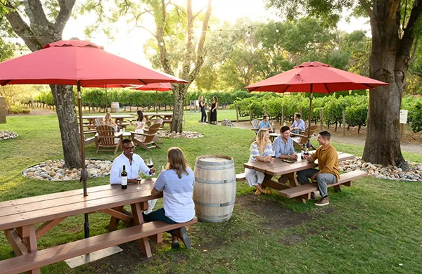 people sitting outside at the Napa Cellars tasting room at picnic tables with red umbrellas drinking wine and having fun