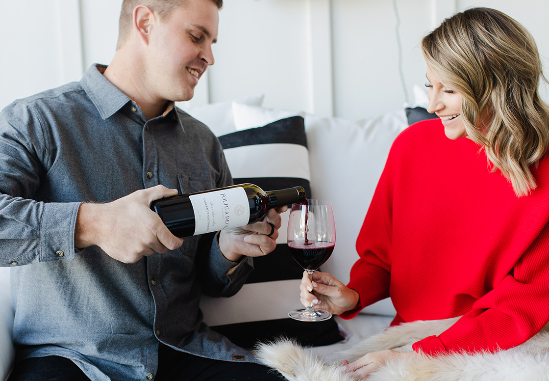 man in a buttondown pouring a woman in a red sweater a glass of folie a deux cabernet sauvignon