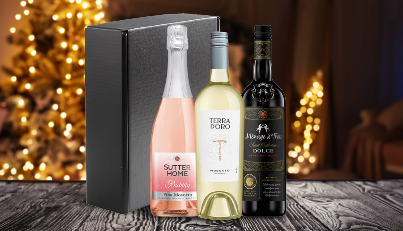 gift box of sutter home pink moscato bubbly, terra d'oro moscato, and menage a trois dolce in front a sparkling tree