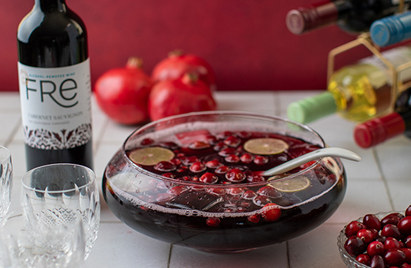 bottle of FRE alcohol-removed cabernet sauvignon next to a bowl of punch with cranberries and lime slices floating in it with glasses off to the side and more FRE alcohol-removed wine bottles in the background