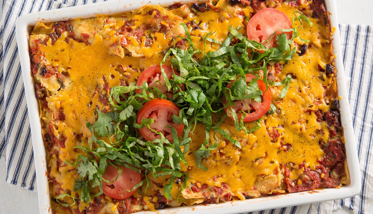 A dish of baked enchiladas covered in cheese and garnished with sliced tomatoes and lettuce.