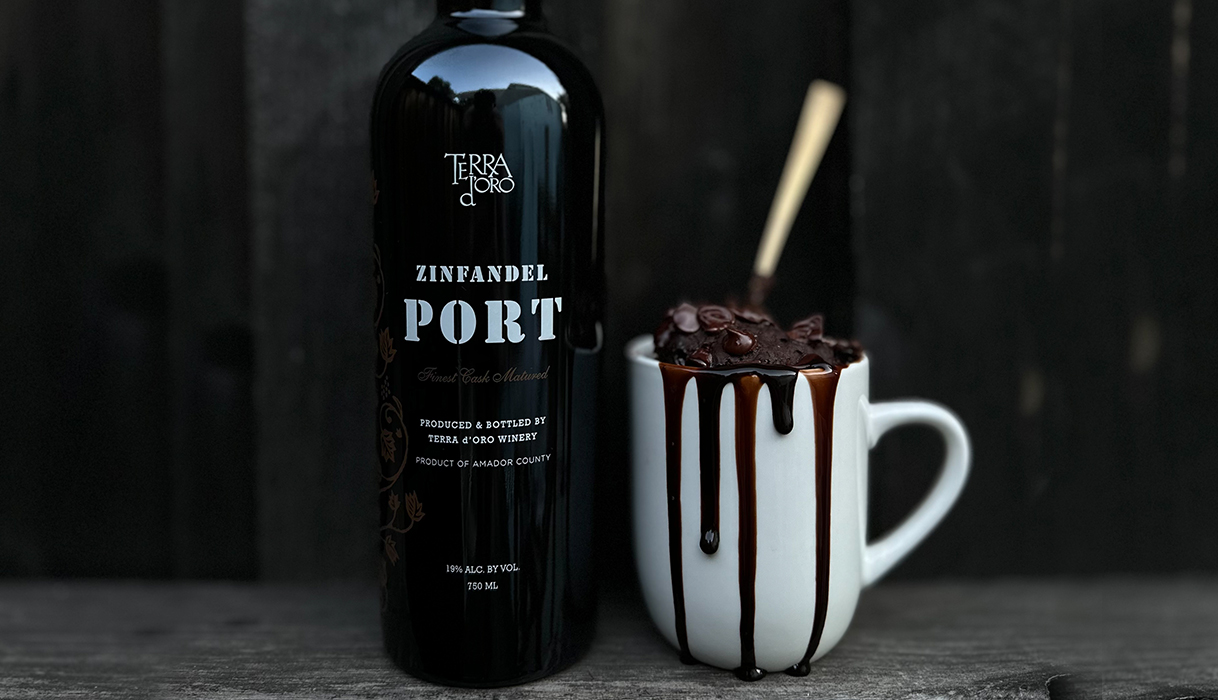 a bottle of Terra d'Oro Zinfandel Port next to a chocolate mug cake oozing with melty chocolate with a spoon inside of it.