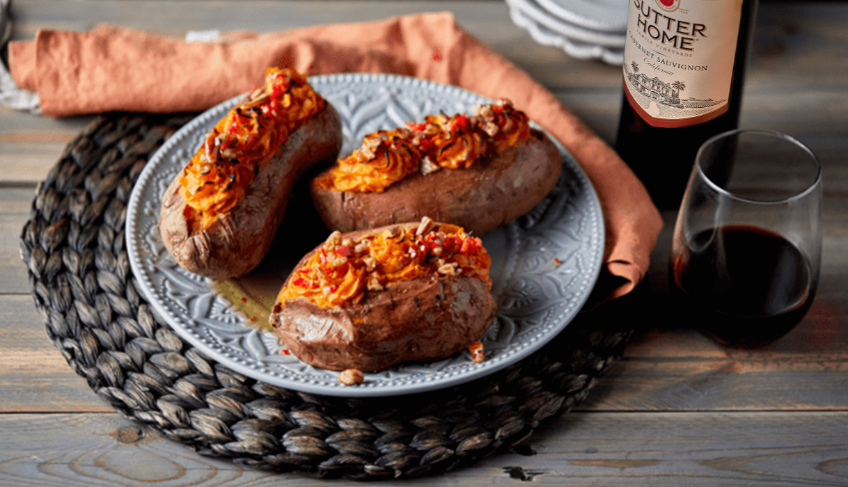 Three twice baked sweet potatoes on a blue plate next to a bottle and glass of Sutter Home cabernet sauvignon